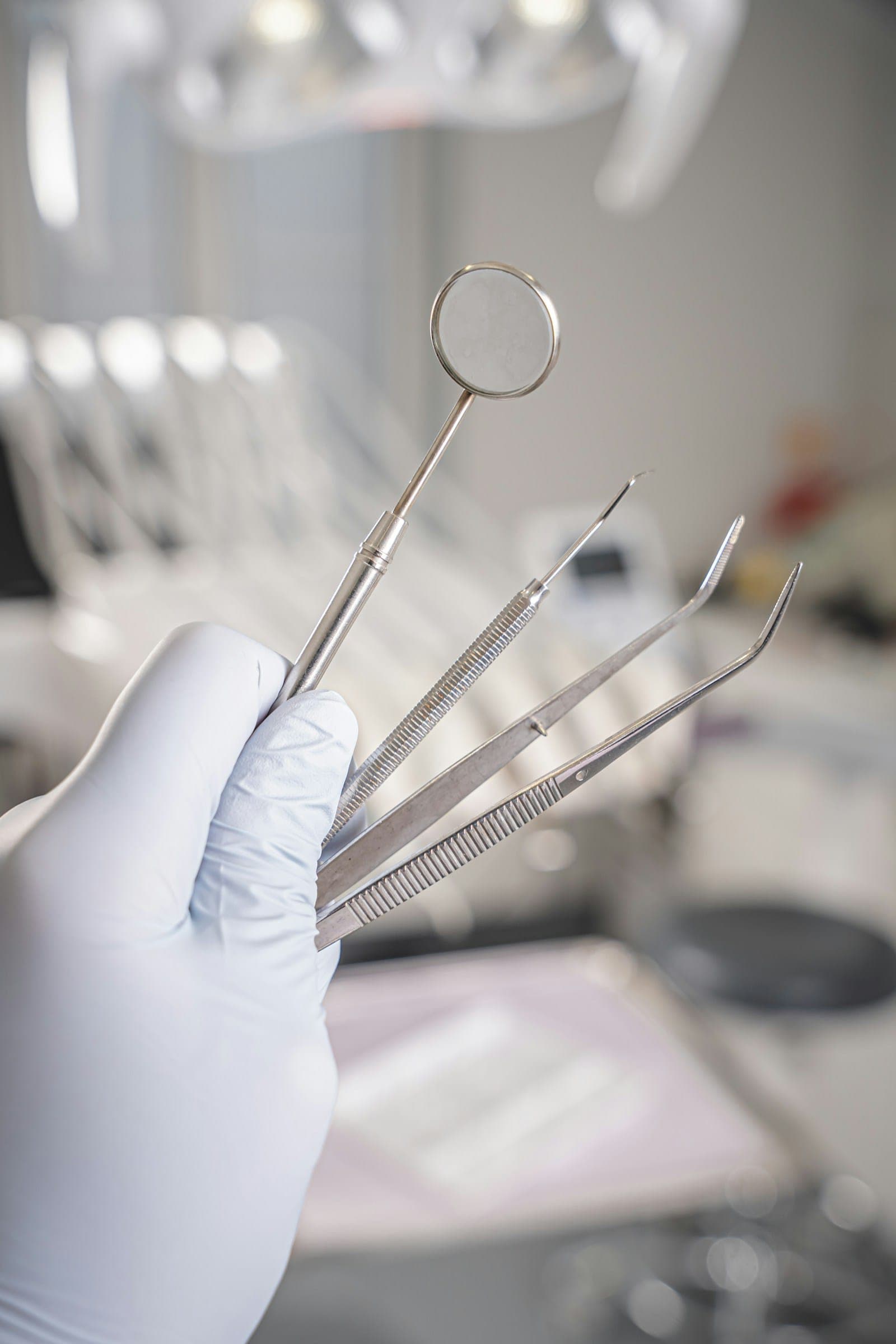 A gloved hand holding stainless steel dental examination instruments
