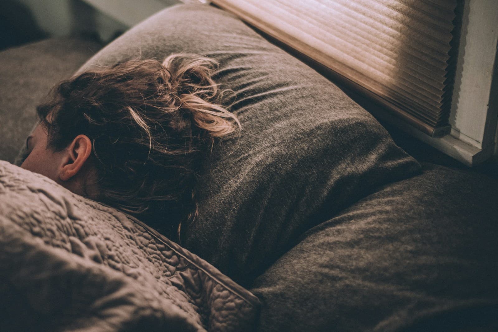 A woman asleep in bed under a gray blanket
