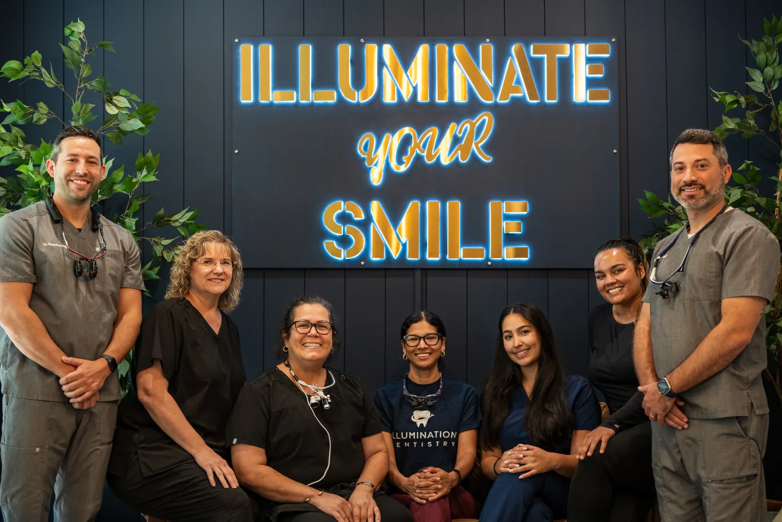 The doctors and staff of Illumination Dentistry standing together in front of the practice's 'Illuminate Your Smile' sign in Lutz, FL